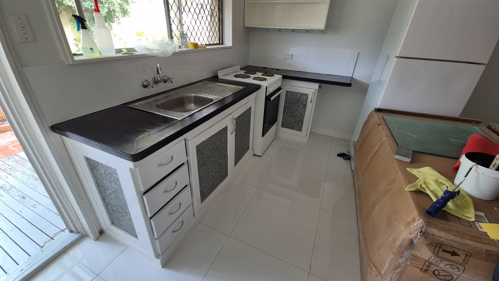 Small kitchen mid-job with cabinets prepared and a roller and paint tin on the bench